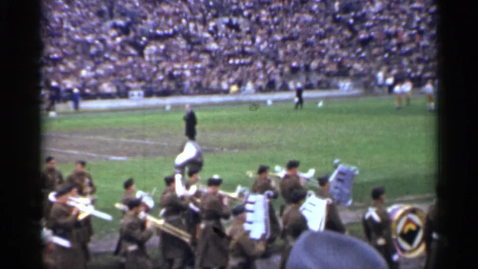 From a spectator angle, uniformed musicians and drum equipment pass along the field edge during the stated 1944 San Francisco stadium ceremony.