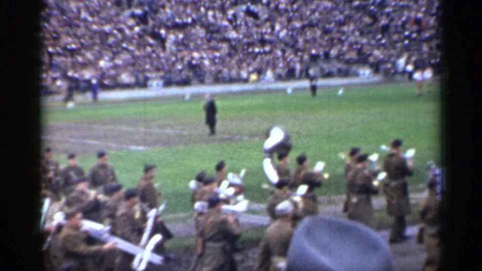 A line of uniformed band members, including a sousaphone player, moves past the camera in the stated 1944 San Francisco stadium footage.