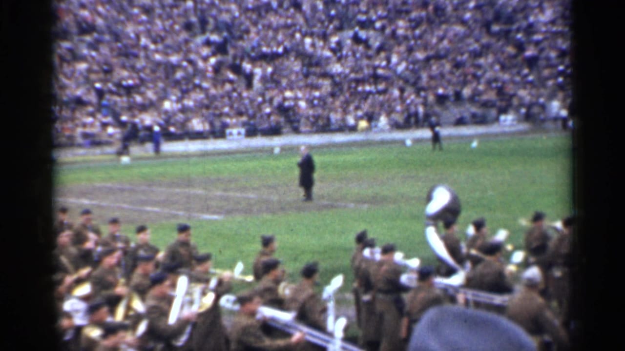1944 San Francisco 8mm frame showing uniformed musicians entering a football field as a large crowd fills the stands.