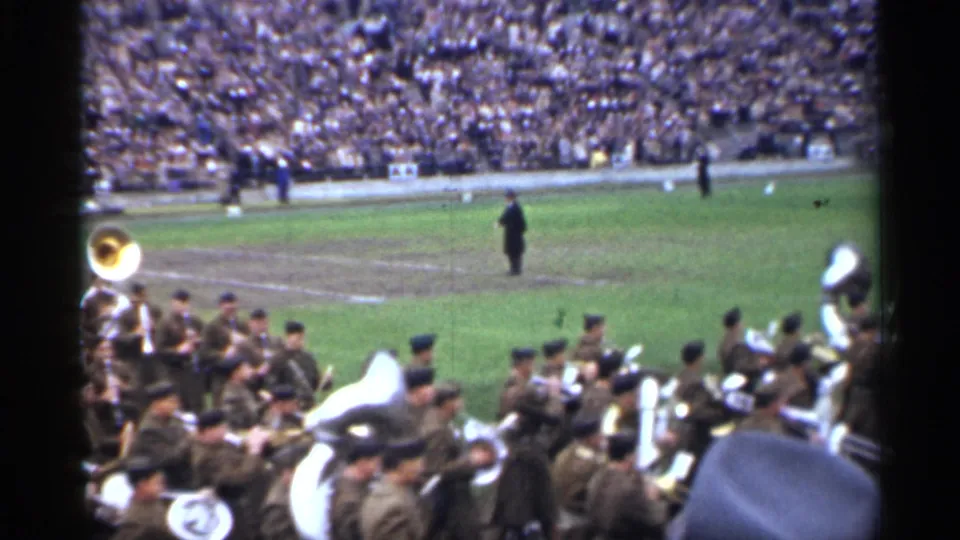 Uniformed military band members with brass and sousaphones march across a San Francisco football field in 1944 footage.