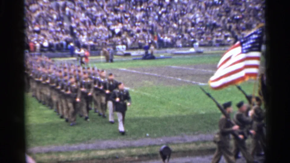 A marching military formation crosses the stadium field in 1944 San Francisco as an American flag fills the right foreground.