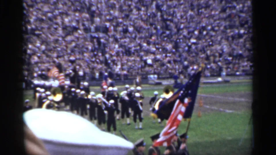 In San Francisco 1944 footage, a marching band in dark uniforms and white caps moves onto a football field before packed stands.