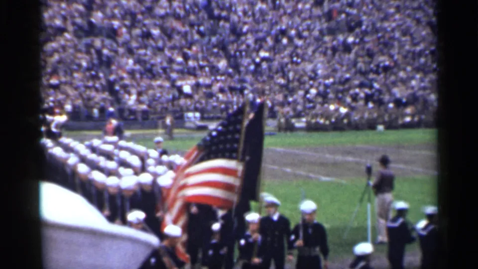 1944 San Francisco 8mm frame showing Navy sailors in formation with an American flag on a stadium field.