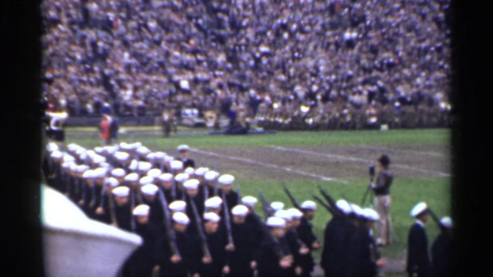 1944 San Francisco 8mm frame showing Navy sailors marching near a field cameraman at a stadium event.