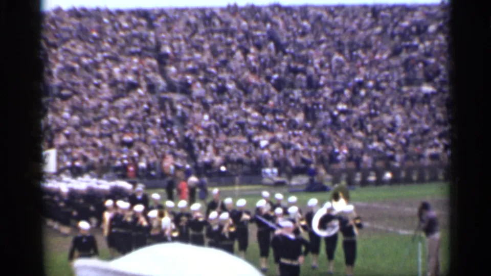 1944 San Francisco stadium frame showing Navy personnel and a marching band moving across the field.