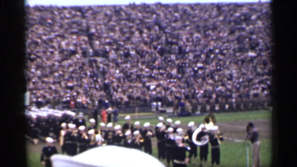 1944 San Francisco 8mm footage shows a dark-uniformed marching band with white hats performing before crowded stadium stands.