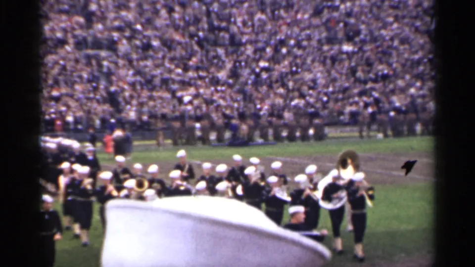 The 8mm frame shows band members in white hats near the field edge, with brass instruments and a crowded San Francisco stadium backdrop.