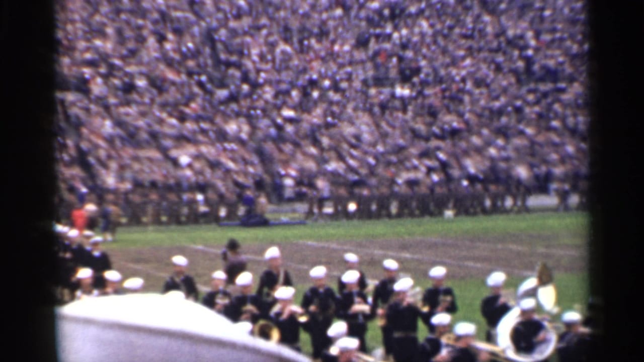 1944 San Francisco home-movie frame of uniformed band members entering a stadium field in front of dense bleachers.