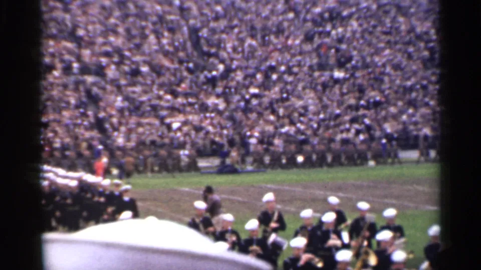 1944 San Francisco 8mm frame showing a military band crossing a stadium field below packed spectator stands.
