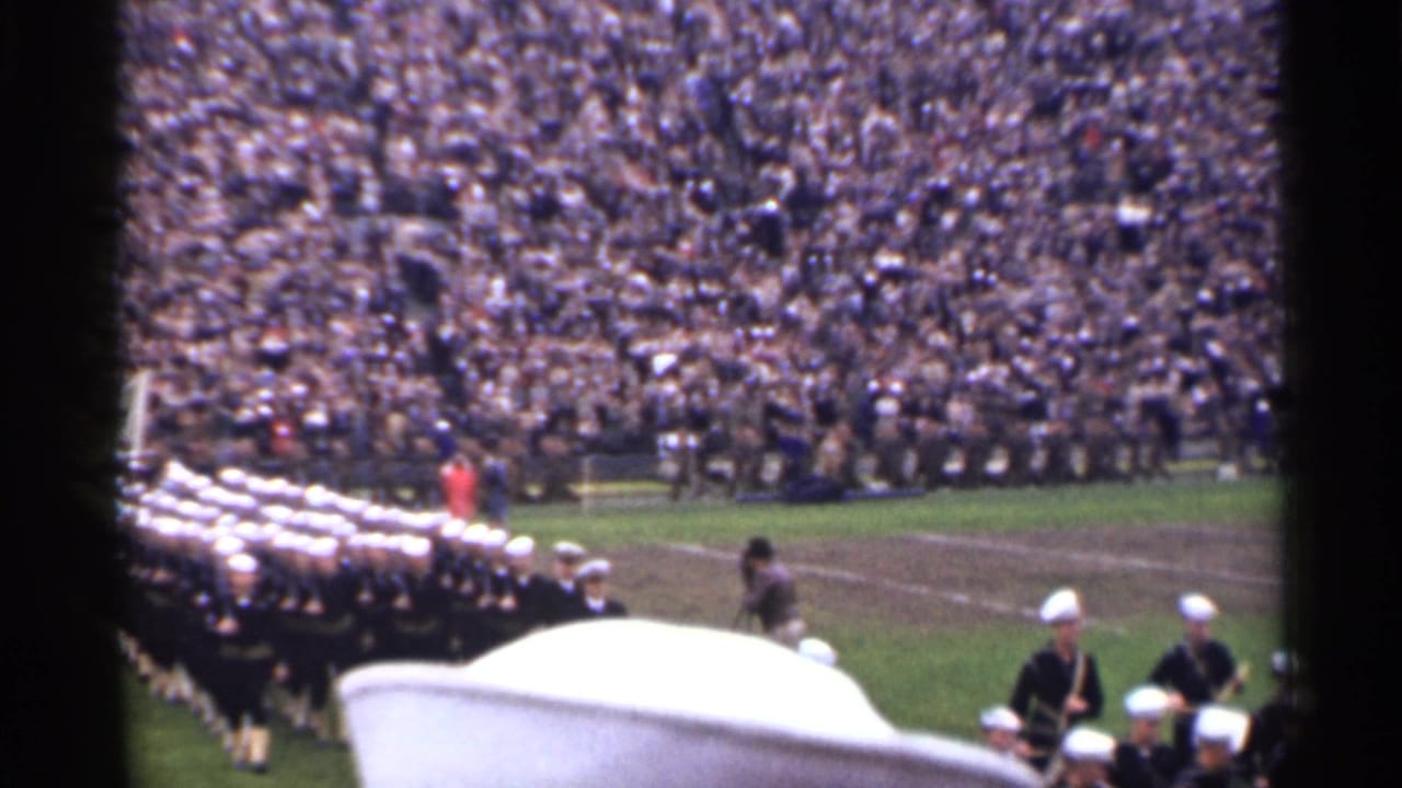 1944 San Francisco 8mm frame showing a marching band formation on a football field with large crowd-filled stands behind it.