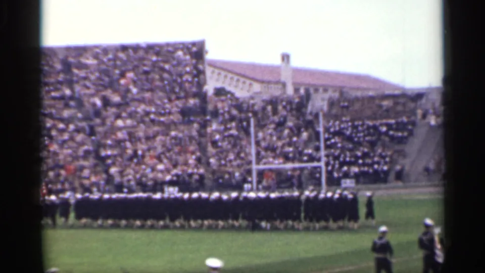 1944 San Francisco home-movie frame showing a marching band near football goalposts with packed stadium seating behind them.