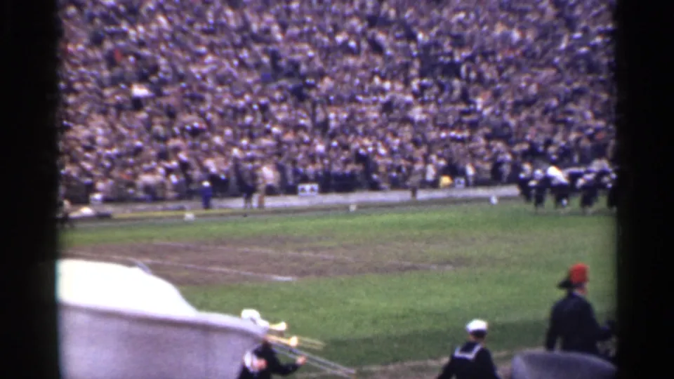 Spectator-shot 1944 San Francisco stadium frame with crowd-filled stands, field activity, and nearby band or audience figures at the bottom edge.