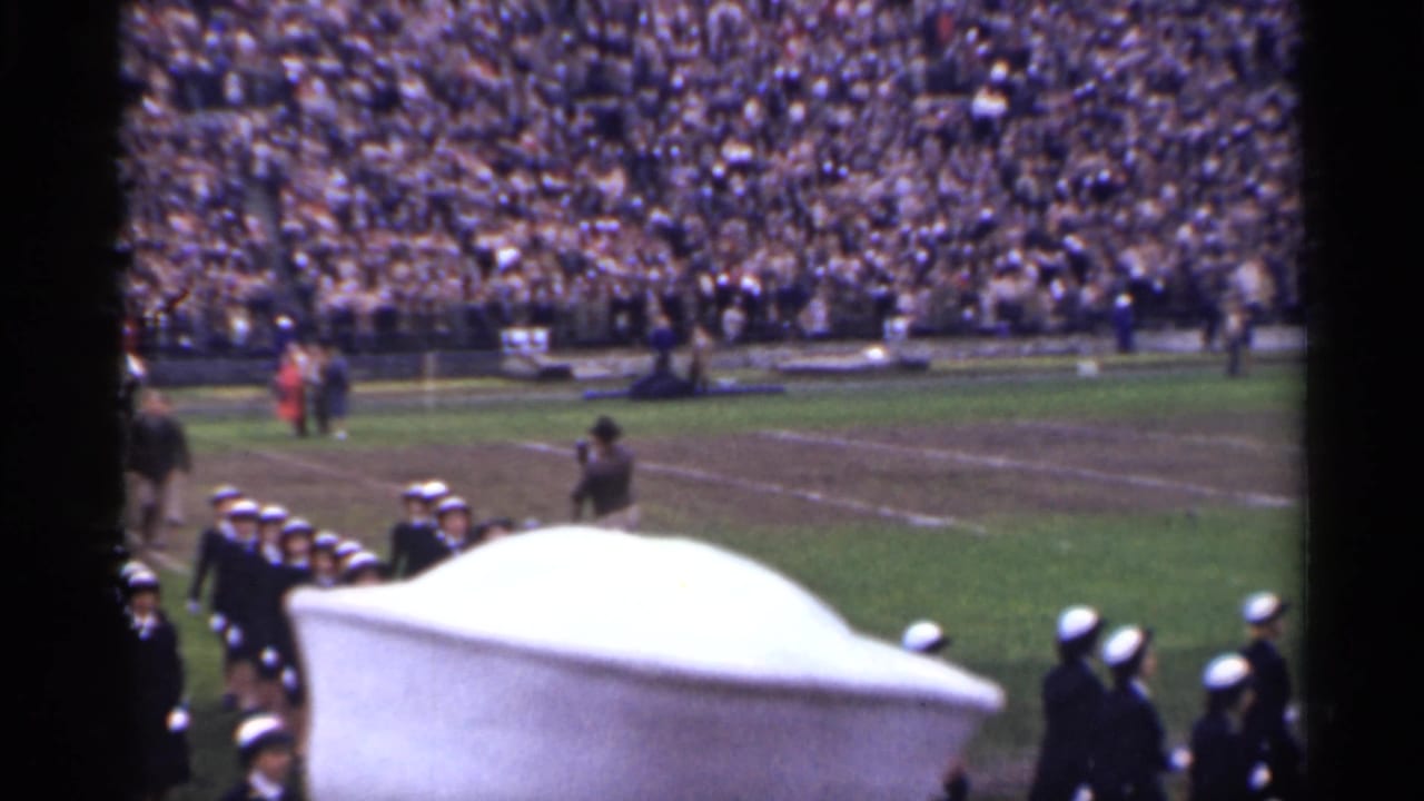 San Francisco 1944 stadium scene with uniformed marchers at the field edge, a large crowd, and handheld 8mm framing.