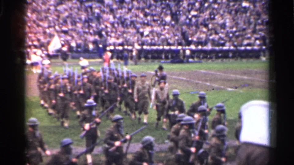Close spectator view of soldiers marching with rifles during a 1944 San Francisco stadium parade, with ranks and crowd visible behind.