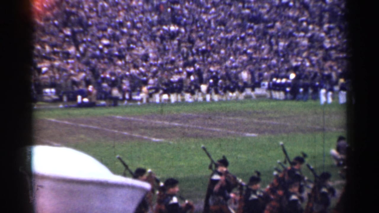 Pipe band in the foreground with a marching band and packed stadium stands beyond.