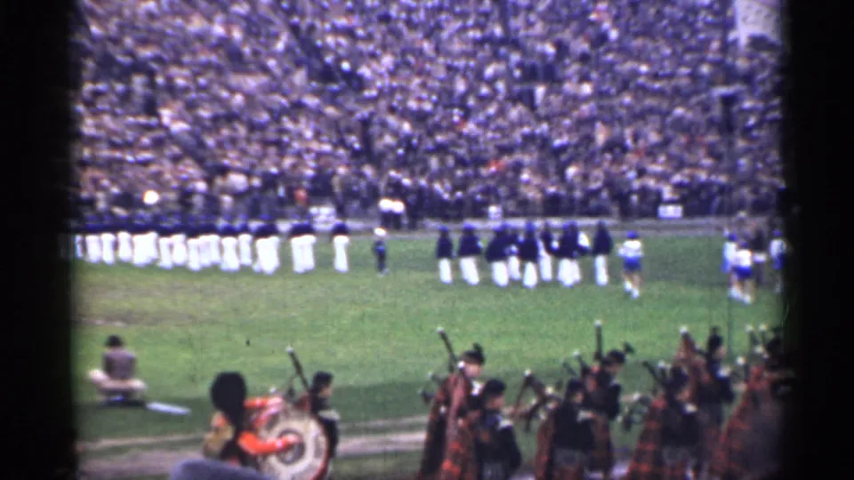Wide 1944 San Francisco stadium frame showing marching band members on the field with pipe band musicians in the foreground.