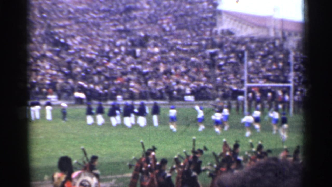 Crowded stadium with band members and football players on the field.