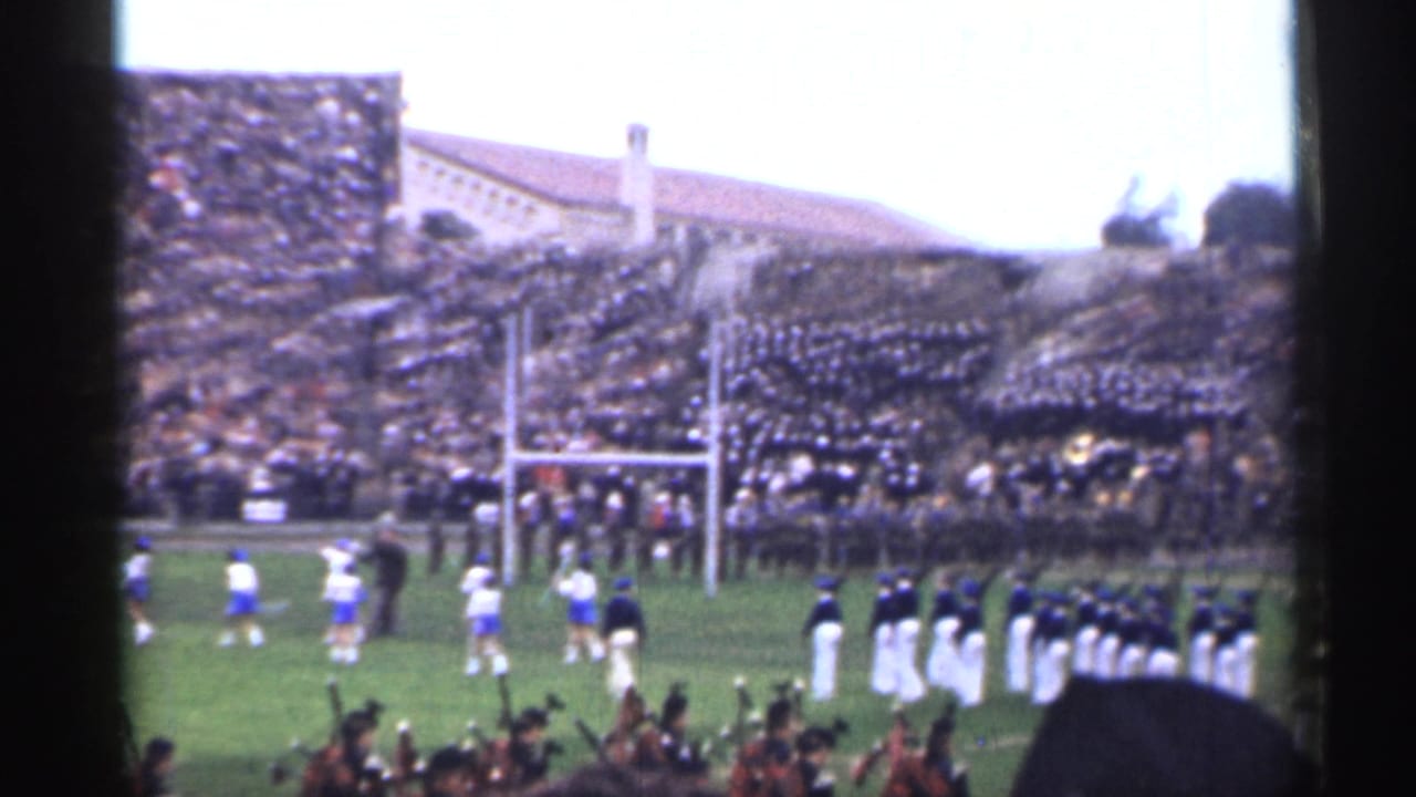 A marching band in white uniforms lines up near the goalpost while blue-and-white players move across the San Francisco stadium field.