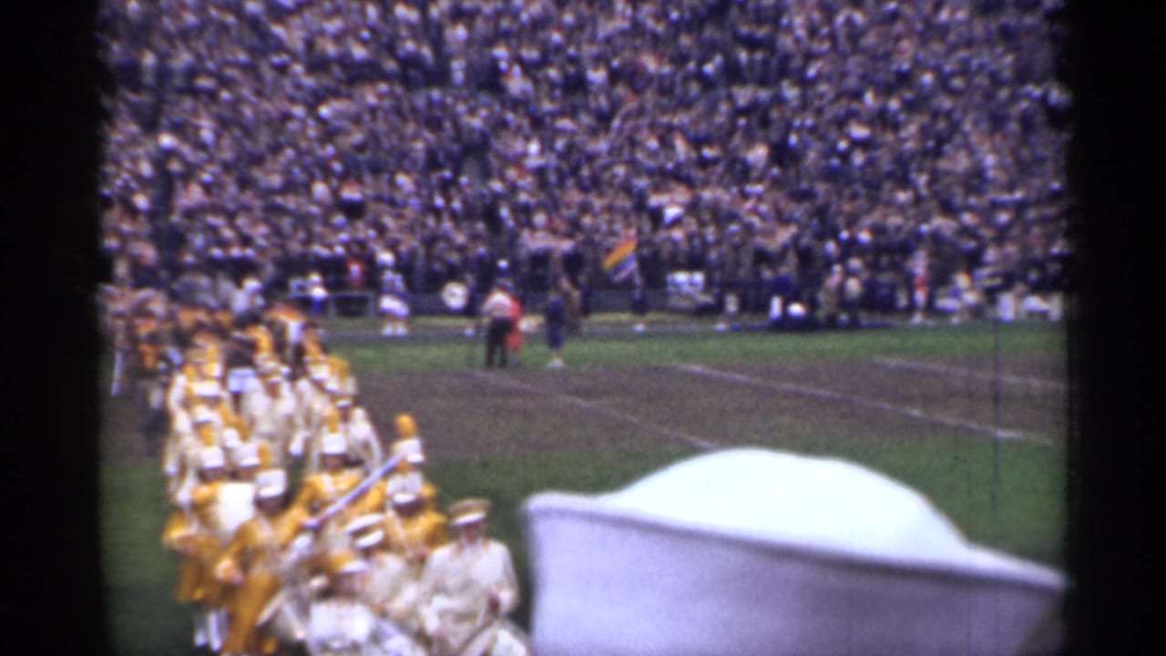 Marching band entering a football field before a packed stadium crowd.