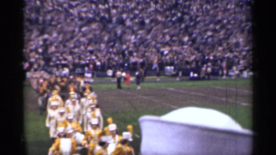 Home-movie frame from a 1944 San Francisco football game showing the marching band closer to the camera amid a large stadium crowd.