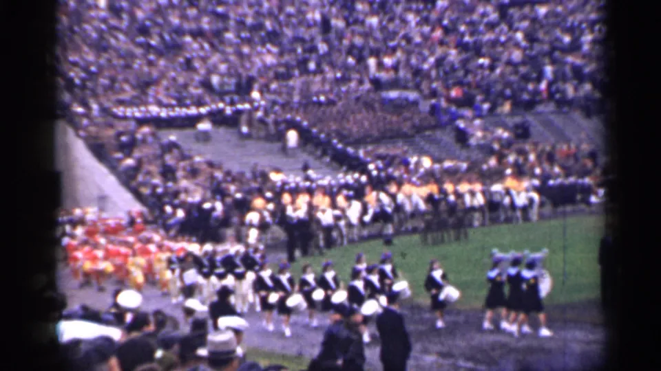 Color 8mm view of a San Francisco football-field procession with marching band sections and a dense stadium audience.