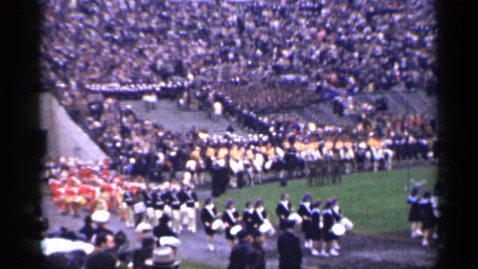 Late frame of the 1944 San Francisco stadium scene with drummers and uniformed marchers crossing near the football field.