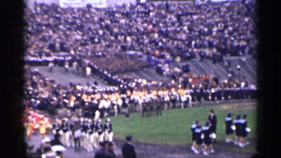 A distant 8mm view shows a marching band, field performers, and crowded bleachers in 1944 San Francisco.