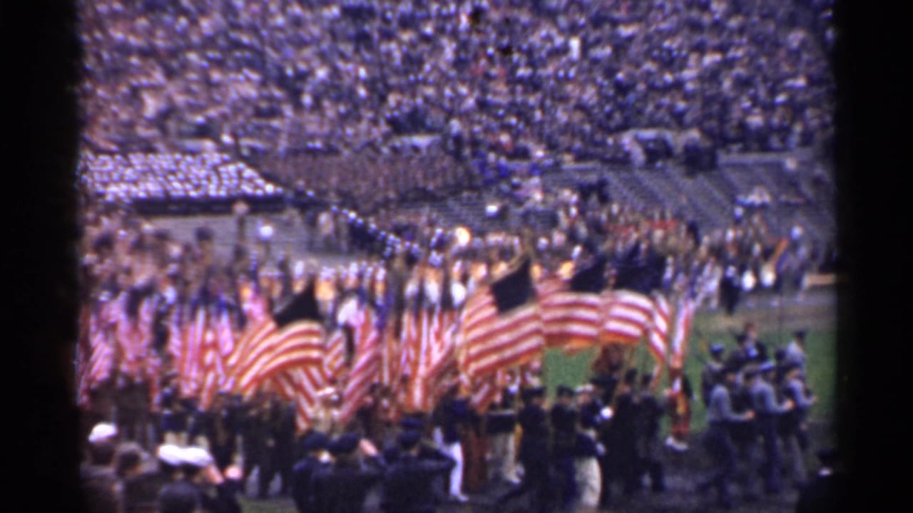 1944 San Francisco home-movie frame showing American flags and uniformed marchers crossing a packed stadium field.