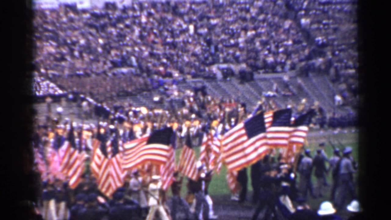 Flag procession and uniformed groups in a crowded stadium.