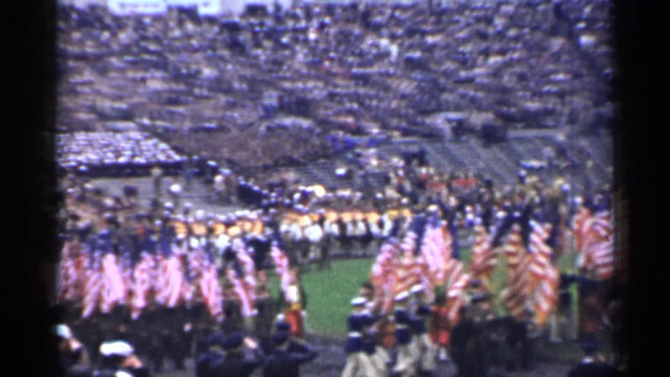 Wide 8mm view of a stadium parade in San Francisco, with American flags, uniformed groups, and crowded stands.