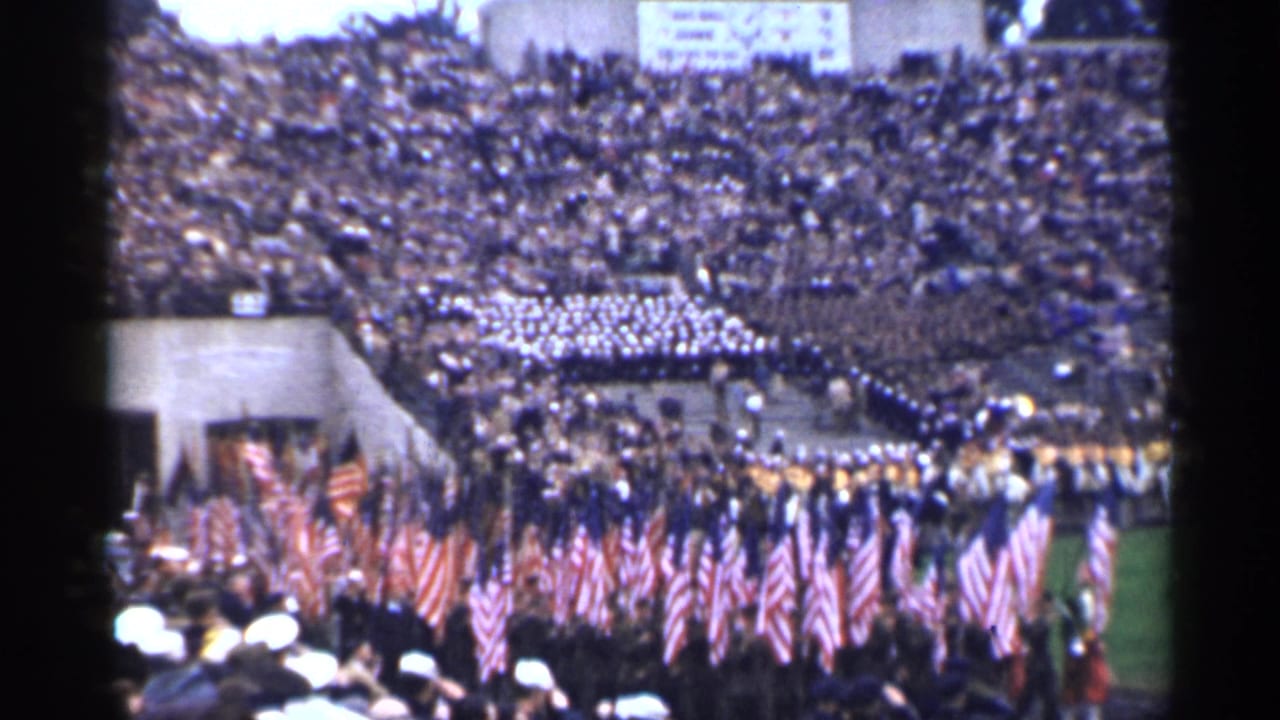 1944 San Francisco stadium scene with flag bearers and uniformed participants moving before a large seated crowd.