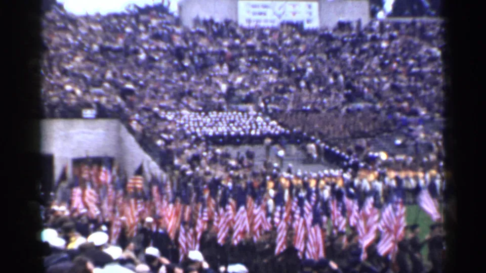 1944 San Francisco 8mm frame of flag carriers and uniformed groups crossing a stadium field before a large audience.