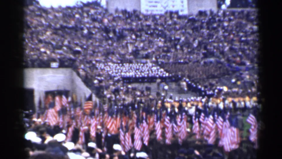 1944 San Francisco home-movie frame showing a broad stadium procession with flags, uniformed marchers, and spectators.