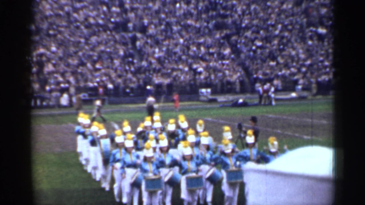 Uniformed marching band performs on a San Francisco football field as a large crowd watches from the stands.