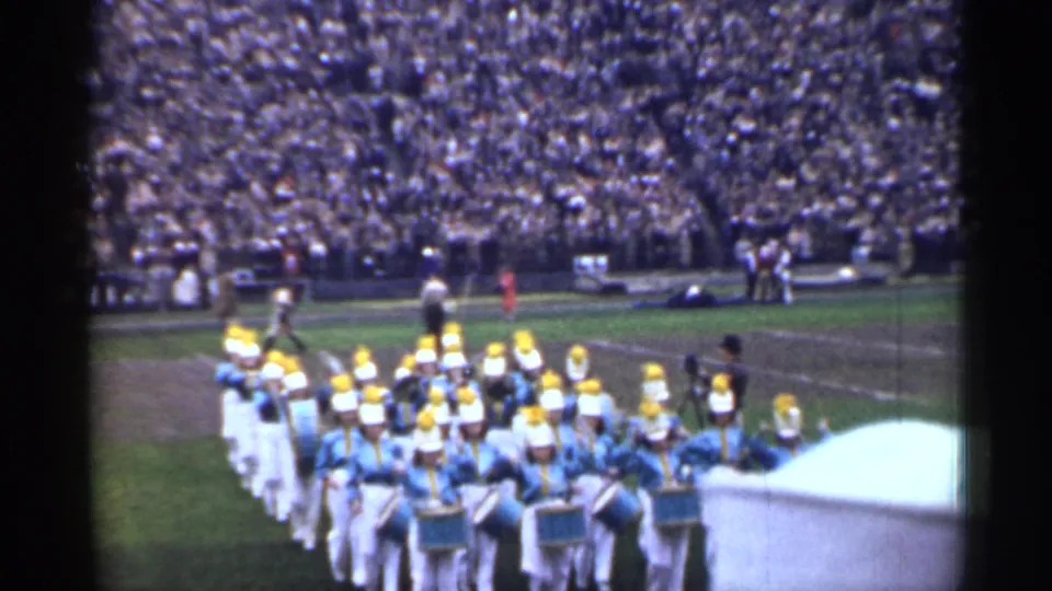Uniformed marching band performs on a San Francisco football field as a large crowd watches from the stands.