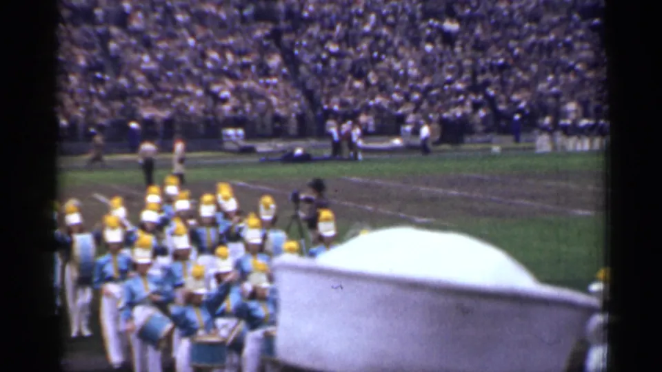 The band gathers near the field edge while spectators fill the background stands in this brief 8mm San Francisco stadium view.