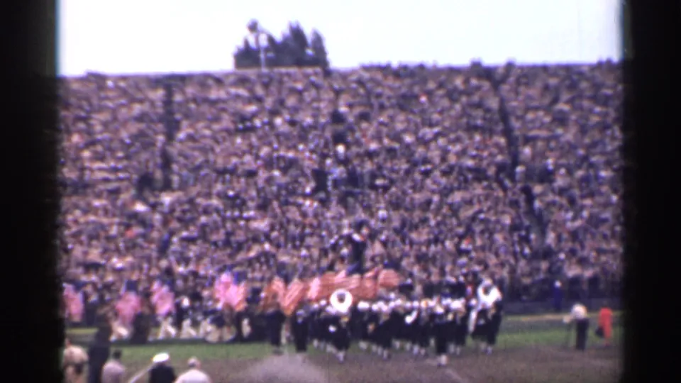 Wide 1944 San Francisco stadium frame with flags, marching formations, and a dense crowd in the stands.
