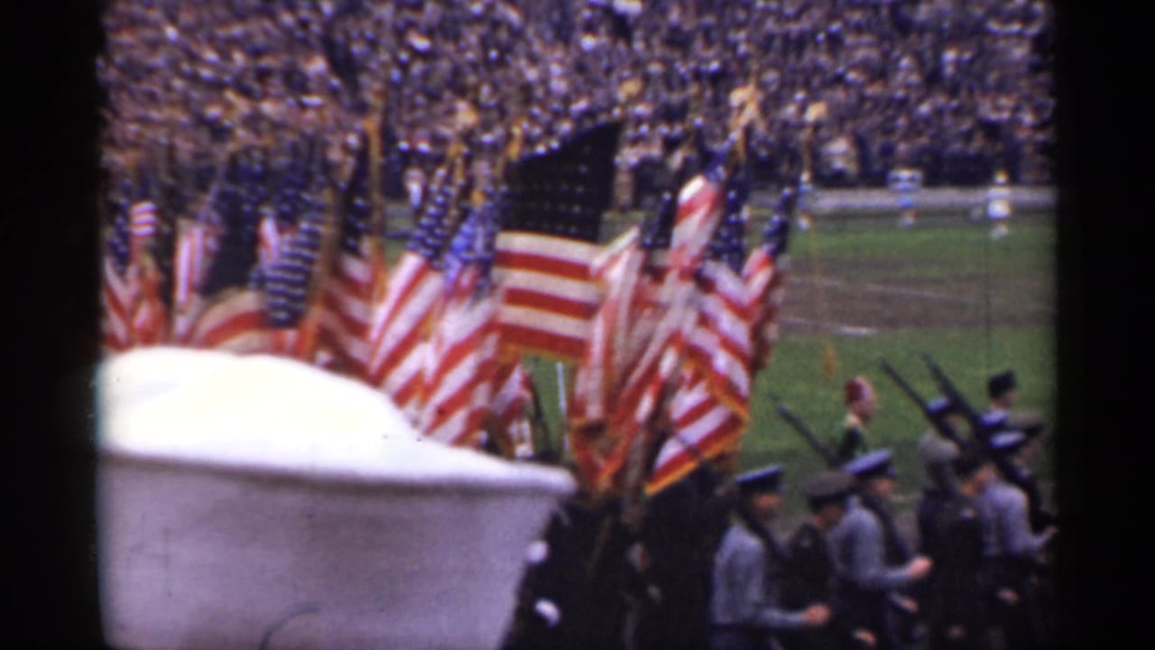 A 1940s San Francisco civic parade view shows flag bearers, uniformed personnel, rifles, and a packed stadium background.