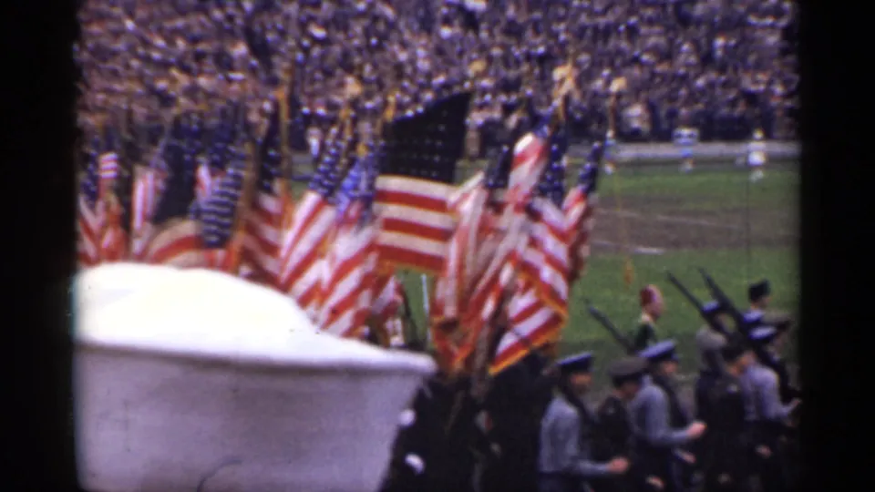 A 1940s San Francisco civic parade view shows flag bearers, uniformed personnel, rifles, and a packed stadium background.