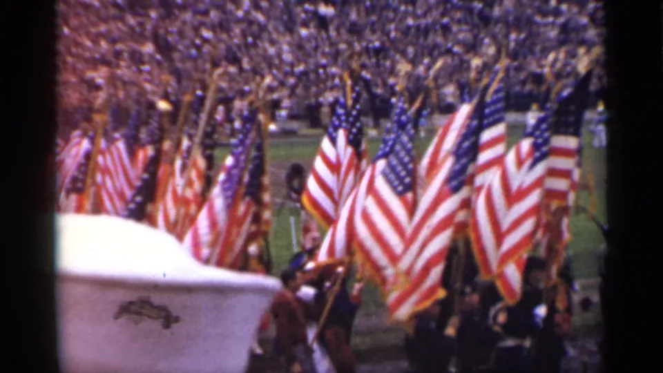 American flags dominate the frame during a 1944 San Francisco patriotic parade, with spectators packed into stadium stands behind them.