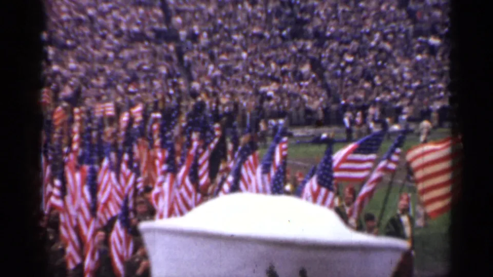 Home-movie view of a dense flag formation during a 1944 San Francisco stadium ceremony, with spectators filling the background.