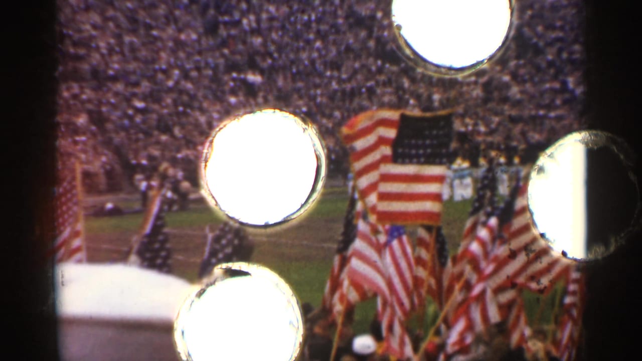 Flags and stadium crowd partially obscured by bright circular film artifacts.