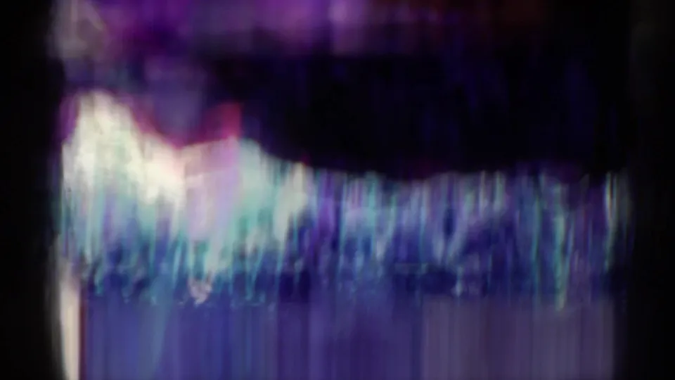 A heavily blurred 8mm frame with color streaking, partial crowd detail, and little readable subject detail from the stadium scene.