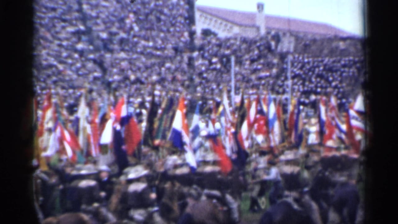 International flags move across a stadium field with horses and spectators nearby.
