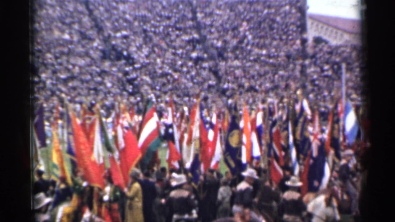 Crowd-filled stadium with many flags gathered near the field edge.