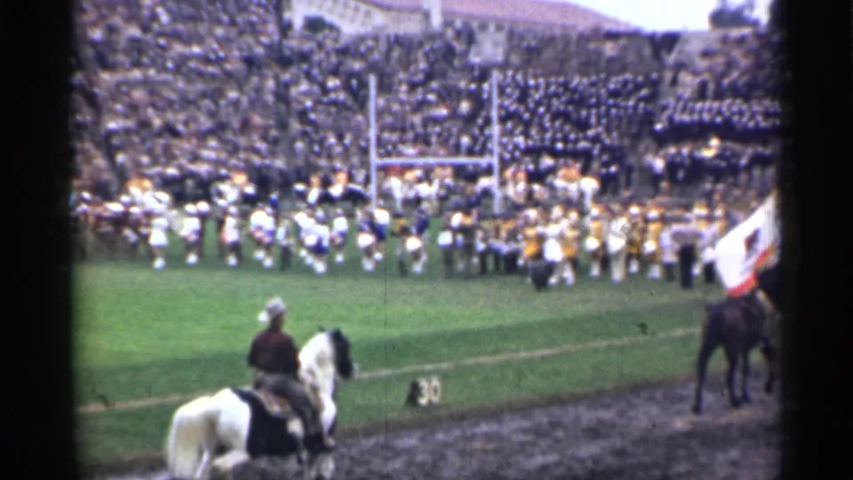 The San Francisco 1944 home-movie frame shows band members across the field, crowded stands, and mounted riders along the stadium sideline.