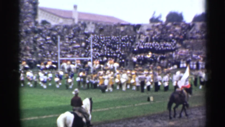 A soft 8mm frame from the 1944 San Francisco event shows marching musicians, a flag at right, riders, and spectators filling the stands.