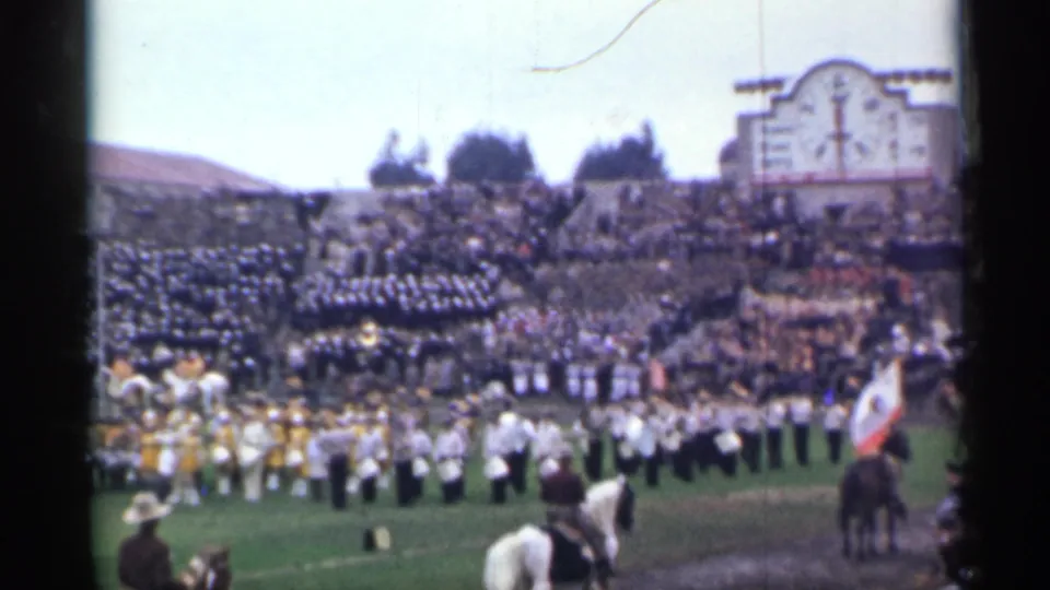 A rider on a light horse appears in the foreground while the marching band, flag bearer, and crowded 1944 San Francisco stadium remain visible.