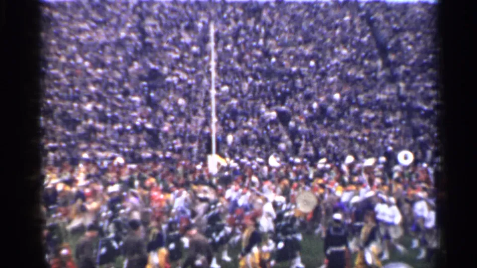 1944 San Francisco home-movie frame showing a crowded stadium, band members, drums, and field movement.