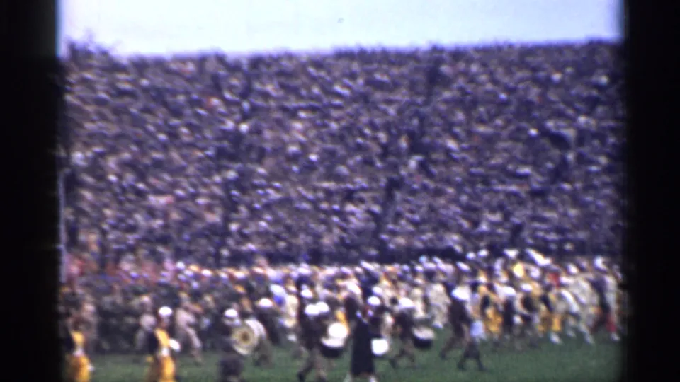 1944 San Francisco 8mm frame showing a marching band with drums and brass on a field before densely filled stadium seating.